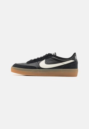 Black athletic shoe with a textured leather upper, white swoosh logo, and a gum rubber sole. Lace-up design with cushioning at the collar.