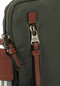 Braune Lederesen auf einer dunkelgrünen, matten Nylon-Tasche mit zwei Reißverschlüssen und goldfarbenen Beschlägen sowie stich-Details.