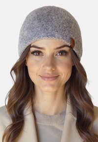 Grå strikket hue med en blød tekstur, der har et lille brunt læderaccentmærke og et glat, rundet krone-design.