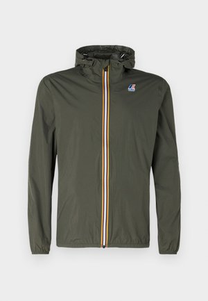 Giacca leggera color verde oliva con cappuccio, dotata di una cerniera frontale con strisce blu, bianche e gialle e un piccolo logo sul petto.