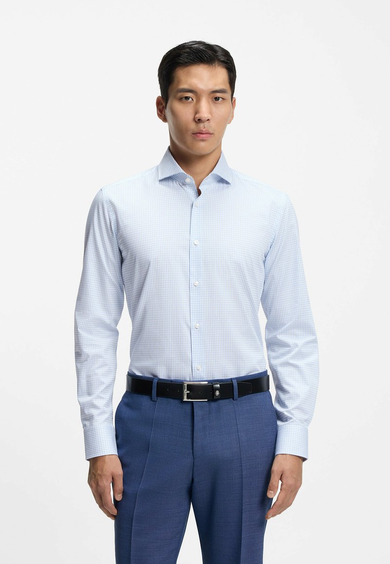 Camicia a quadri azzurri con maniche lunghe e colletto appuntito, abbinata a pantaloni blu e cintura nera.