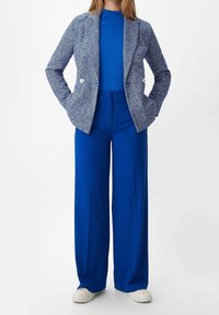 Modrý tvídový blazer se dvěma knoflíky, zkombinovaný se solidním modrým žebrovaným topem a širokými modrými kalhotami. Outfit doplňují bílé tenisky.