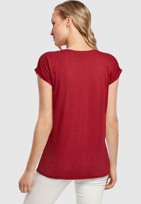 Rød t-shirt med korte ærmer, buet nederkant og opfoldede ærmer, lavet af et blødt stof. Bagfra ses en afslappet pasform.