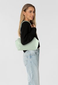 Licht mintgroene leren handtas met een gestructureerd ontwerp, korte dubbele handvatten en een fluweelachtige textuur. Voorzien van een ritsluiting en minimalistische styling.