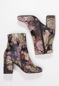Bottes noires pour chevilles avec des motifs floraux brodés en or, rose et violet. Dotées d'un talon épais et d'une fermeture éclair latérale.