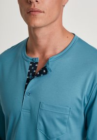 Teal shirt met lange mouwen en een henley-kraag, met een gestreepte marineblauwe knoopsluiting en een borstzak. Glad materiaal met een ontspannen pasvorm.