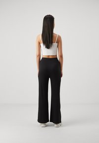 Pantalon large côtelé noir, taille haute, associé à un débardeur blanc court. Modèle vu de dos, cheveux lisses et foncés.