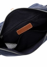 Offene navyblaue Reißverschlusstasche, die das Innenfutter aus Stoff, eine interne Reißverschlusstasche und ein braunes Leder-Brandlabel zeigt, das innen eingenäht ist.