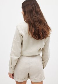 Vaalean beige pellavapaita pitkillä hihoilla, takana johto-ompelus, yhdistettynä vastaaviin korkeavyötäröisiin shortseihin, joissa on käänteet.