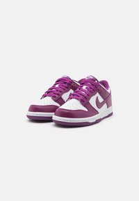 Une paire de baskets Nike basses avec des panneaux en cuir blanc et violet et des lacets violets sur un fond blanc uni.
