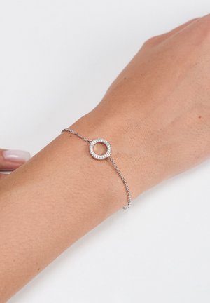 Zilveren armband met een cirkelvormige hanger met heldere strasstenen, bevestigd aan een fijn kettinkje, liggend op een licht getinte huid.