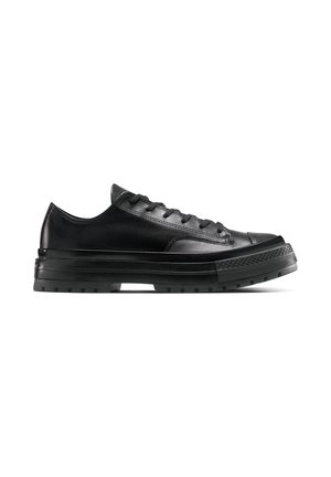 Zapatilla negra de piel baja con suela gruesa de goma, cordones delanteros y puntera texturizada, mostrada de lado sobre fondo blanco.