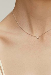 Collarín de cadena de plata con un pequeño colgante cuadrado. La cadena presenta un diseño de eslabones delicado, descansando sobre la piel suave en la clavícula.