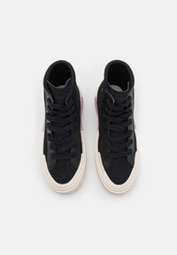 Černé vysoké tenisky s texturovaným svrškem, šněrovacím designem, kontrastní krémovou gumovou podrážkou a jemnými purpurovými akcenty po straně.