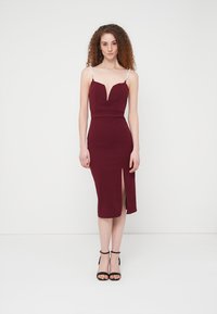 Βουργουνδί εφαρμοστό φόρεμα με βαθύ ντεκολτέ, πλευρικό σκίσιμο και λεπτές τιράντες με χάντρες. Λείο, ελαστικό ύφασμα, σχέδιο μέχρι το γόνατο.