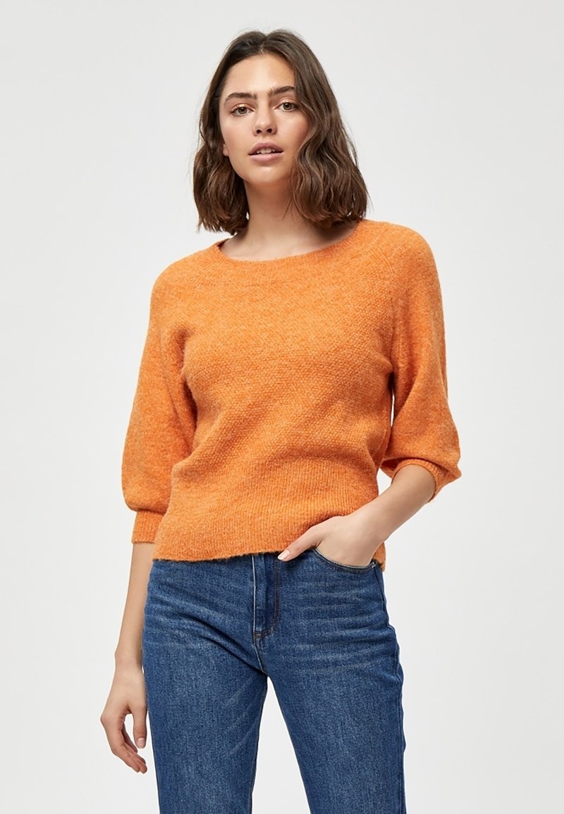 Maglione arancione lavorato a maglia con scollo rotondo, maniche a tre quarti e tessuto strutturato. Abbinato a jeans in denim blu.