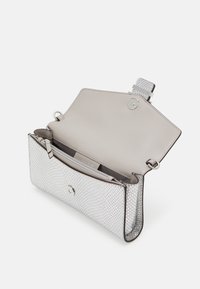 Hopeahipun messinki, jossa on sileä kermaisen valkoinen sisustus. Varusteena magneettinen lukitus, pieni tasku ja tyylikäs, rakenteellinen muoto.