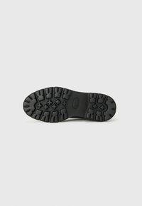 Semelle de chaussure en caoutchouc noir avec des bandes de roulement profondes et des motifs croisés. Présente une surface lisse avec un logo au centre. Construction durable.