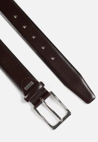 Ruskean nahkavyö, jossa on sileä pinta, hopeanvärinen metallikenkä, useita säätöreikiä ja suorakulmainen metallikoriste.