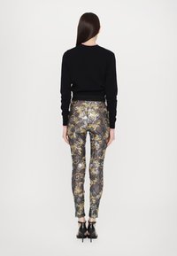 Svart genser med rosa detaljer, parret med metallisk mønstrede leggings med gull- og sølvakenter, avsluttet med svarte høyhælte sko.