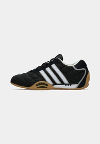 Pantofii de fotbal în interior Adidas negri cu dungi albe, talpă din cauciuc, textură matlasată și șireturi, prezentați din profil lateral pe fundal alb.