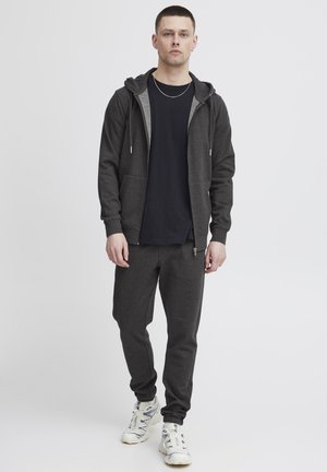 Dark gray hoodie with a contrasting inner lining, paired with matching joggers. Worn with a dark shirt and white athletic shoes.