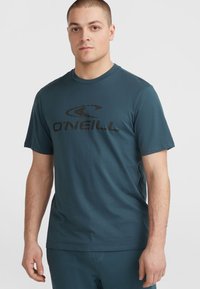 Tīrā zila kokvilnas T-krekls ar melnu O'Neill logotipu, kas centrēts uz krūtīm. Īsas piedurknes, apaļa kakla izgriezums un brīvs piegriezums.