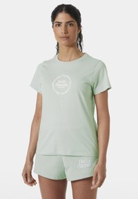 Camiseta de algodón verde claro con mangas cortas, cuello redondo y logo circular de Helly Hansen en el frente; combinada con pantalones cortos a juego.
