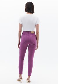 Jeans ajustados de tejido rosa vibrante, con cintura alta, bolsillos traseros y una etiqueta de cuero marrón en la cintura. Combinados con un top corto blanco.