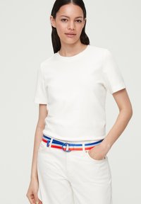 T-shirt blanche à manches courtes avec un col rond, assortie à un pantalon de couleur claire. Ceinture rayée multicolore avec une boucle circulaire très visible.