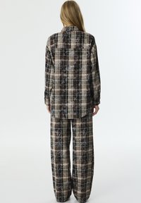 Set di abbigliamento loungewear a quadri nei toni marrone, beige e nero. Camicia dal taglio rilassato con colletto e maniche lunghe, abbinata a pantaloni ampi. Tessuto morbido.