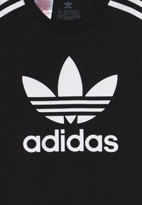Svart t-shirt med en stor vit Adidas-logga som har en trebladig design och tre horisontella ränder på axlarna.
