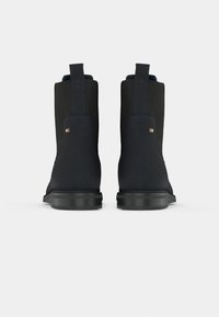 Et par sorte ankelstøvler med trækklogger og små logo-tags på bagsiden, vist fra bageste vinkel mod en hvid baggrund.