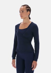 Granatowa, długorękawowa bluzka zapinana na zakładkę z kwadratowym dekoltem i miękką fakturą. Charakteryzuje się dopasowanym krojem oraz delikatnym, krzyżującym się detalem z przodu.