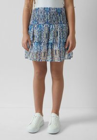 Gelaagde rok met een smock-buikband in een blauw-wit abstract patroon, gecombineerd met witte sneakers.