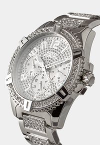 Sudraba pulkstenis ar teksturētu ciparnīcu, rotāts ar akmentiņiem ap malu un siksniņu. Tam ir vairāki ciparnīcas un izteiksmīgi stundu rādītāji.