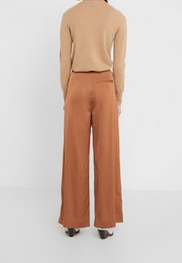 Wijduitlopende, roestkleurige broek van gladde stof. Heeft een achterzak en een hoogtaille ontwerp, gecombineerd met een beige trui.