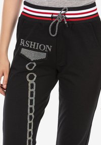 Schwarze Jogginghosen mit einem gestreiften Bund, verziert mit Strasssteinen und dem Wort "FASHION" in Silber, im Kettenmuster-Design.