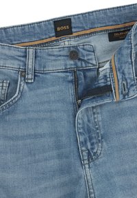 Slim fit blue denim jeans with a zip fly, button closure, and a black label featuring "BOSS." Visible stitching and pockets highlighted.
