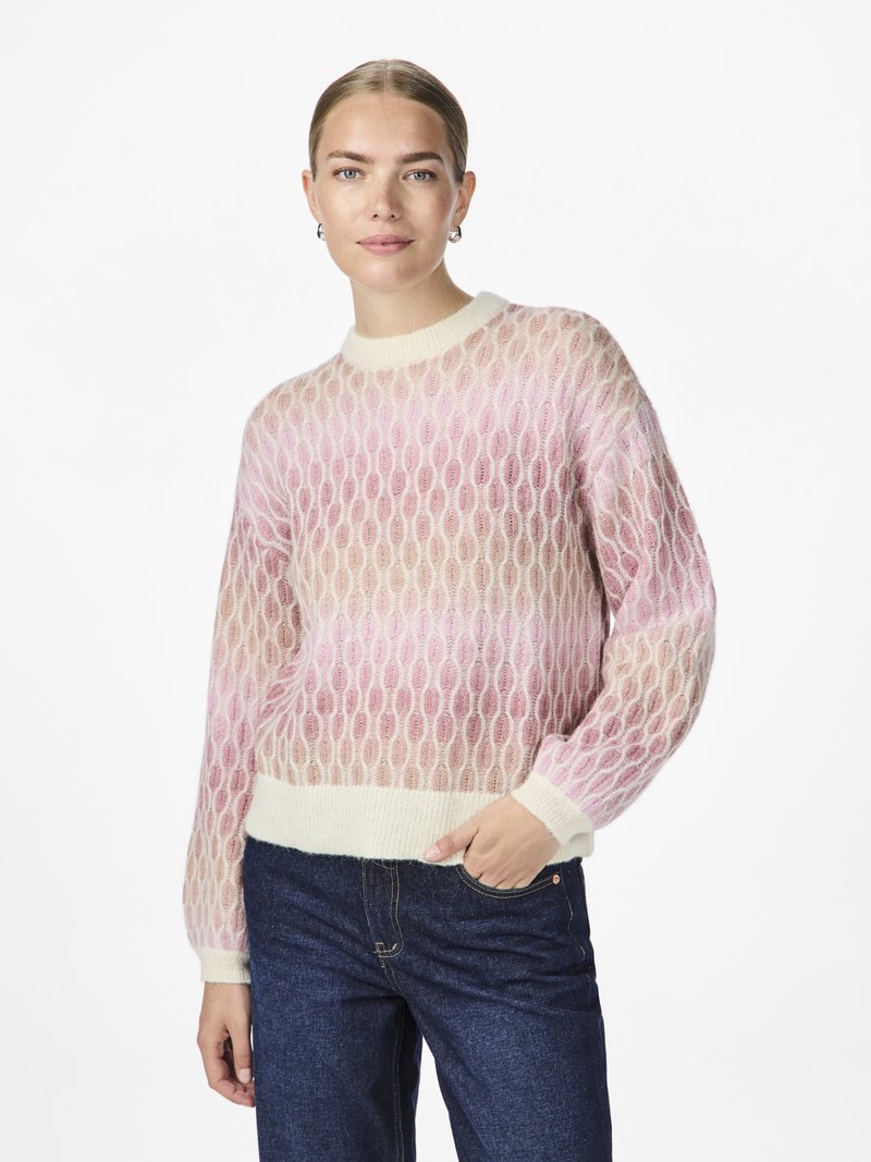 Strikkegenser i lys rosa og krem med et mesh-mønster, ribbestrikkede mansjetter og nederkant. Brukt sammen med mørke denimjeans.