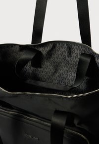Borsa a spalla nera con esterno liscio, chiusura con cerniera e interno con motivo di iniziali ripetute. Presenta due manici in tessuto.