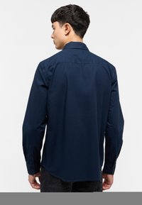 Camisa de manga larga azul marino con cuello abotonado, dobladillo recto y puños abotonados, que presenta una textura de algodón suave.