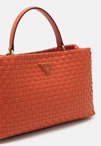 Oranžová wovaná kabelka se strukturovaným tvarem, vybavená trojúhelníkovou zlatou logem a pevným horním držadlem, vyrobená z texturovaného materiálu.