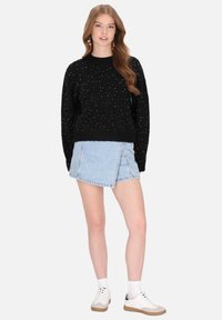 Fekete kötött pulóver színes pöttyökkel, kerek nyakkivágással és bordás mandzsettákkal. Világoskék farmer rakott szoknyával és fehér sportcipővel párosítva.