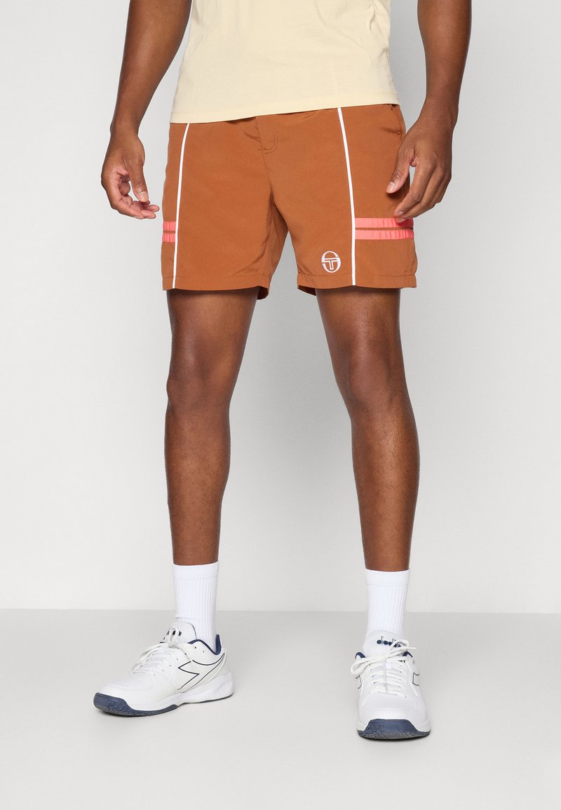 Mænds brune badebukser med hvide side-striber, lyserøde detaljer og logo. Stoffet ser let og hurtigttørrende ud. Båret med hvide træningssko.