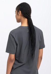 Grijze T-shirt met korte mouwen en een ontspannen pasvorm, met een schaarafbeelding op de achterkant van de nek. Zachte katoentextuur, minimaal design.