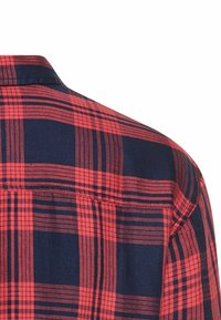 Een rood en marineblauw geruite overhemd met een kraag, zichtbare naaddetails en een gestructureerd stofpatroon met horizontale en verticale lijnen.
