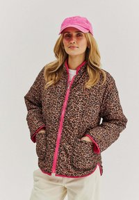 Kurtka puchowa w print w panterkę z różowym zamkiem i wykończeniem, z bocznymi kieszeniami i luźnym krojem. W połączeniu z różową czapką.
