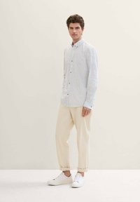 Camisa de botones a rayas en azul claro y blanco, combinada con pantalones beige entallados y zapatillas blancas. Textura suave y ajuste relajado.