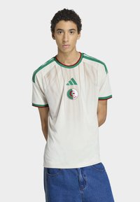 Wit sportshirt met groene accenten en rode bies. Heeft een geperforeerde textuur en het embleem van het Algerijnse nationale team op de borst.